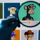 A person holding a lens up to a screen with a bored ape NFT on the screen.
